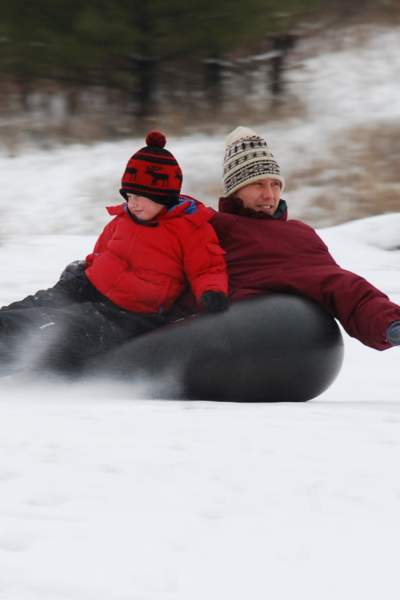 A man and a boy snowtubing on Mount Hoy