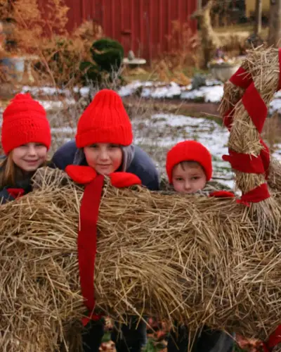 Three children hide behind a festive hay sculpture