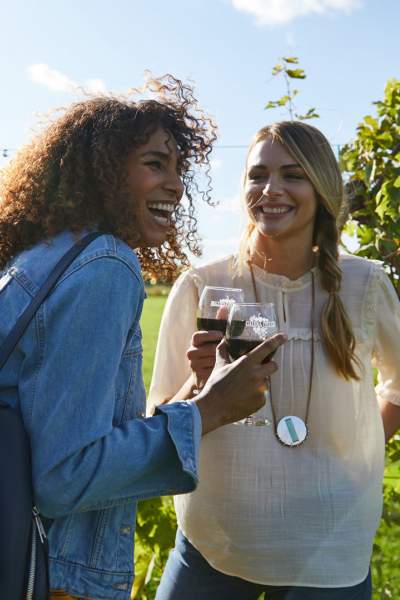 Two girls laugh while enjoying red wine at a vineyard