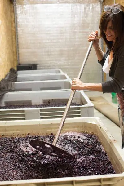 A woman mixing the grapes in a large container to make wine.