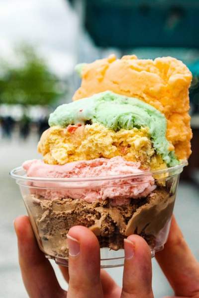 Close up of a colorful ice cream in a clear plastic bowl, being held in someone's hand.