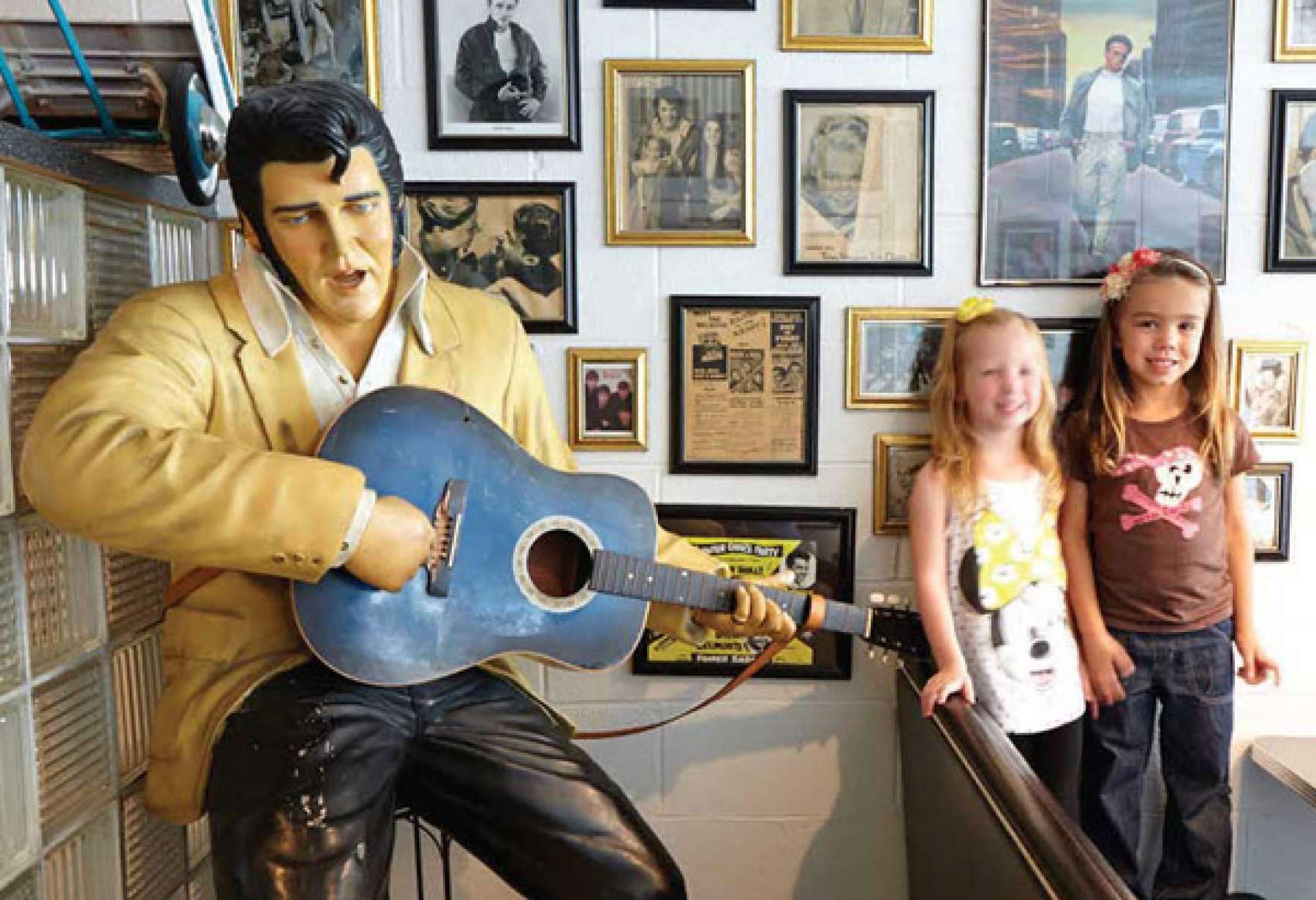 Two young kids getting a photo next to a statue of Elvis Presley holding a guitar 