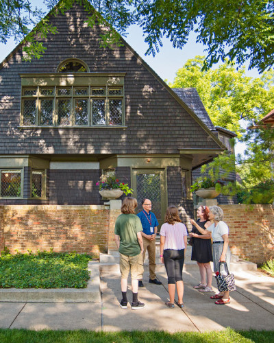 A guide speaks to a tour group on the sidewalk in front of Frank Lloyd Wright's house and studio in Oak Park