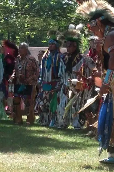 A group of men in Native American attire on a grass clearing amid trees