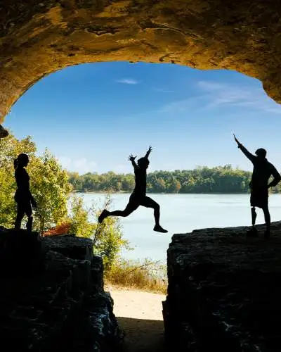 A person jumps across a rock with friends, blue sky and water in the background