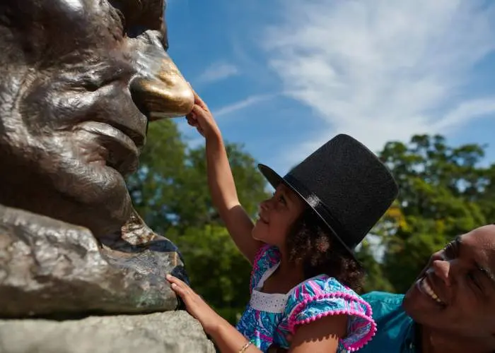 Father lifting up his daughter to touch the nose of the Lincoln statue.