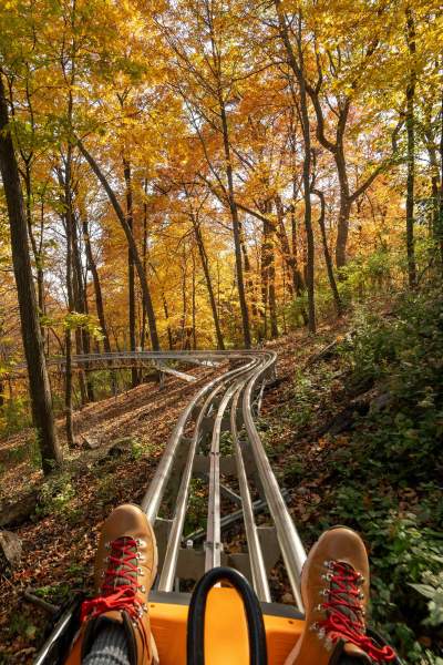 View of feet and coaster as person rides the Alpine Coaster through fall foliage at Aerie's Resort Grafton