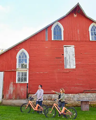 A couple on bikes in front of a red barn