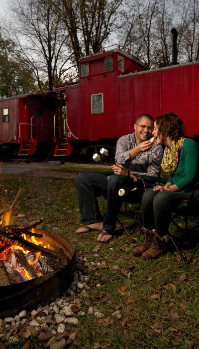 Couple toasting marshmallows on the bonfire with a train behind them.