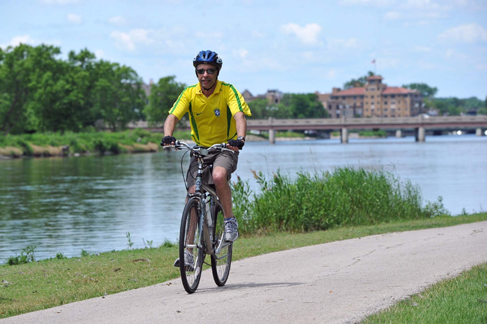 A man in a bright yellow shirt cycling on a path next to the Fox River