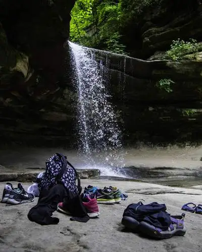 A waterfall from a rock, with peoples bags and shoes lying on the rock below