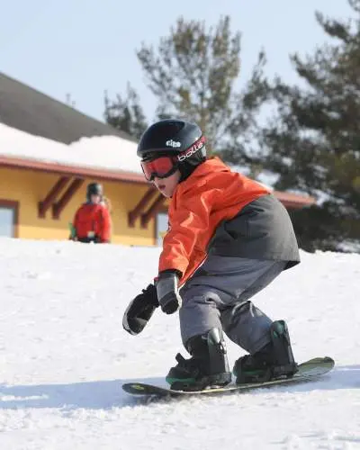 A small child riding a snowboard on snow, wearing a helmet, goggles, and warm ski clothing