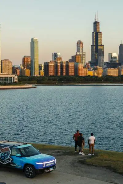 Three people stand admiring the Chicago skyline with a Rivian EV vehicle