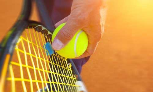 A close up of someone getting ready to serve a tennis ball